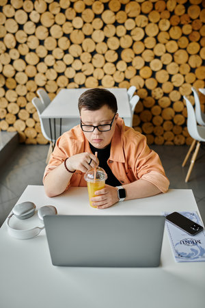 A man with down syndrome sits in a cafe, working on his laptop and enjoying a refreshing drink.の写真素材
