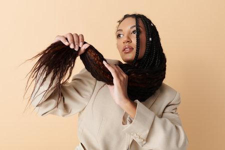 A young woman with long black braids poses against a neutral background, wearing a light-colored blazer and a thoughtful expression.の写真素材