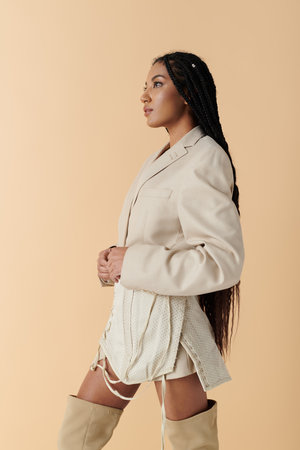A stylish African American woman in her 20s poses in a beige blazer and mini skirt against a neutral background.の写真素材