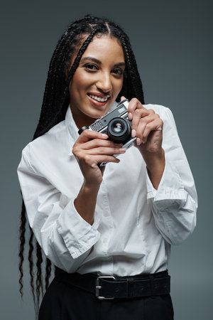 A young woman with long black braids smiles as she holds a vintage camera.