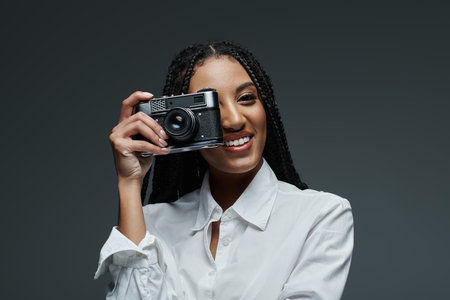 A stylish woman with braided hair smiles while holding a camera in front of her face.の写真素材