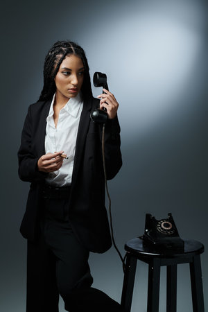 A young woman in a black suit holds a vintage phone receiver and gazes intently into the distance.の写真素材