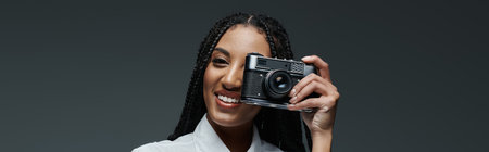 A young woman with long braids smiles brightly as she holds a vintage camera to her eye.の写真素材