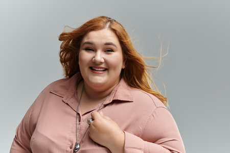 A plus-size woman with red hair smiles confidently, her windblown hair adding movement to the image.の写真素材