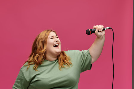A woman with long red hair sings into a microphone in front of a pink backdrop.