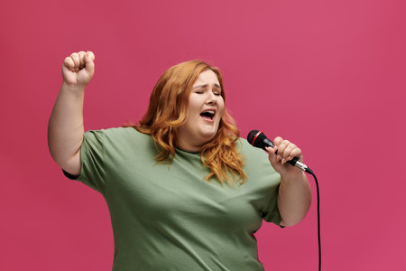 Plus size woman with long red hair sings into a raised arm carrying a microphone