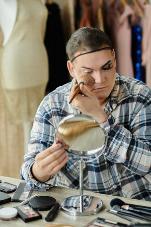 queer person uses makeup with brushes in front of a mirrorの写真素材