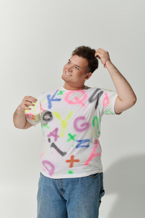 A queer person smiles brightly, wearing a white t-shirt covered in colorful graffiti.