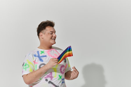 A queer person in a colorful shirt holds a rainbow flag, smiling brightly.の写真素材
