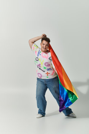 A smiling queer person holds a rainbow flag, radiating joy and confidence.の写真素材
