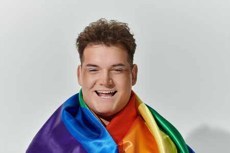 A queer person draped in a rainbow flag smiles broadly.の写真素材
