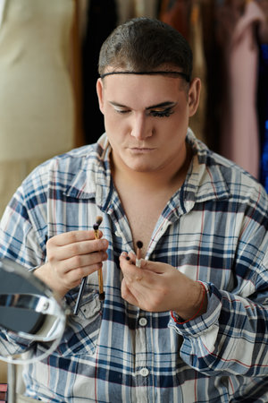 A queer person applying makeup while holding two brushes.