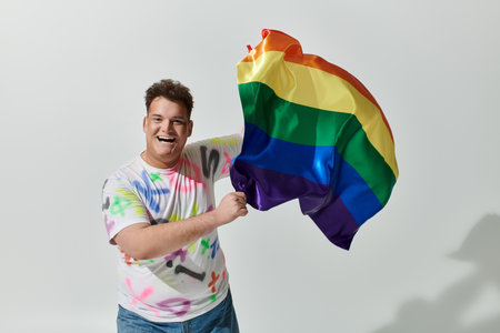 A man smiles brightly as he holds a rainbow flag high.の写真素材