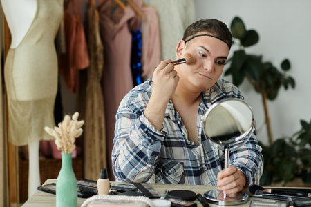 A queer person applies makeup in a room with a mirror and makeup brushes.の写真素材
