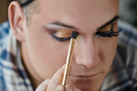 A close-up of a queer person applying eye shadow with a brush.の写真素材