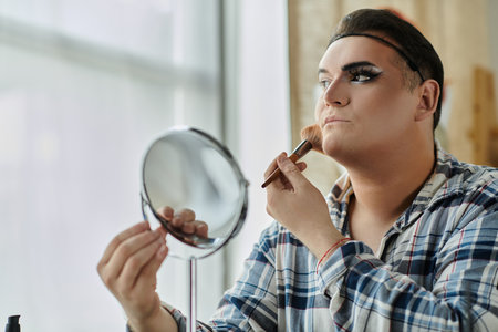 A queer person applies makeup in front of a mirror, focusing on their face.の写真素材