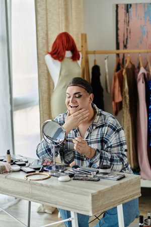 queer person applies makeup in mirror amid beauty productsの写真素材