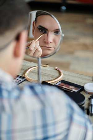 A queer person applies eyeliner with a brush, looking intently in a mirror.の写真素材
