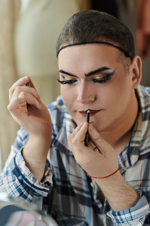 A queer person applies lip liner while wearing stylish attire.の写真素材