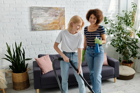 Two women vacuum and clean their modern apartment together, laughing and enjoying their time.の写真素材