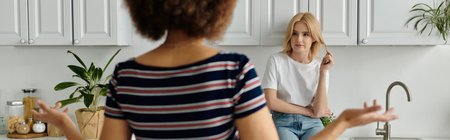 Two women argue in a kitchen, one with her back turned, hands gesturing, the other seated, looking away.の写真素材