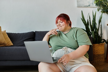A plus size woman sits on a couch, thoughtfully looking at a laptop.の写真素材