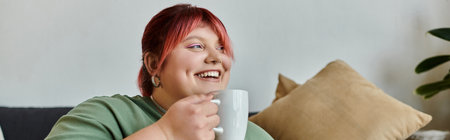 A woman with pink hair smiles and enjoys a drink while sitting on a couch.の写真素材