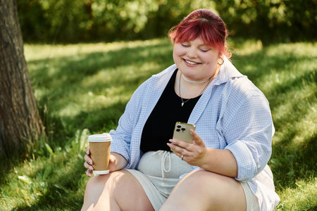 Woman with pink hair smiles, enjoys coffee in park, scrolls phoneの写真素材