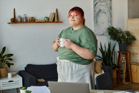 A woman stands in her home office, holding a mug and looking thoughtfully.