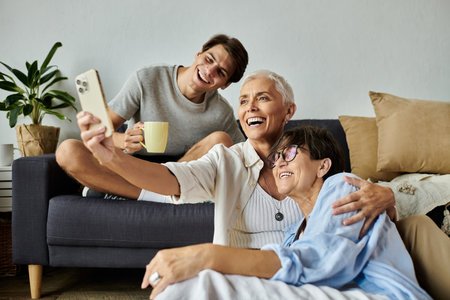 Lesbian parents and their adult son share laughter and smiles while taking a cozy selfie at home.