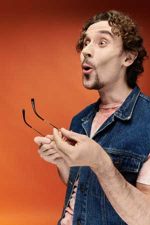 A surprised man with curly hair joyfully holds sunglasses, showcasing lively emotions.