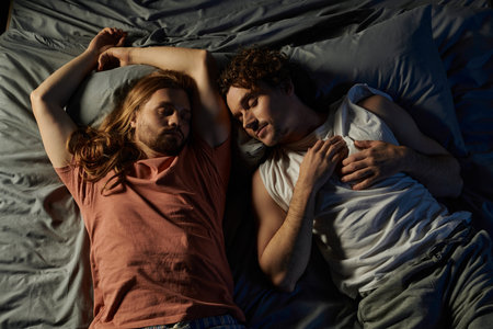 Two partners share an intimate moment lying together in bed at home.の写真素材