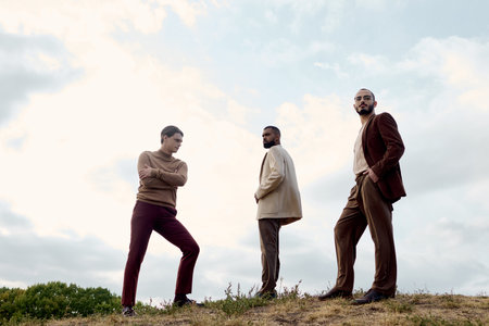 Three handsome men showcase fashionable autumn attire while standing in a picturesque field during fall.の写真素材