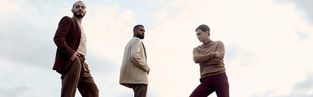 Three handsome men dressed in elegant autumn attire enjoy a moment in a picturesque natural...