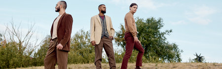 Three handsome men elegantly pose in fashionable autumn outfits amidst a picturesque field setting.
