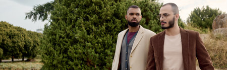 Two handsome men showcase fashionable autumn attire while enjoying nature beauty in the field.