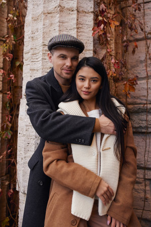 A couple enjoys a tender embrace, surrounded by autumn foliage in their cozy outfits.の写真素材