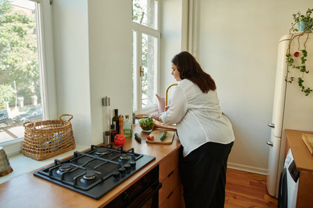 A confident woman happily chopping vegetables by the window.の写真素材