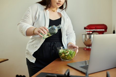 A cheerful woman mixes a colorful salad with a hint of olive oil at home.