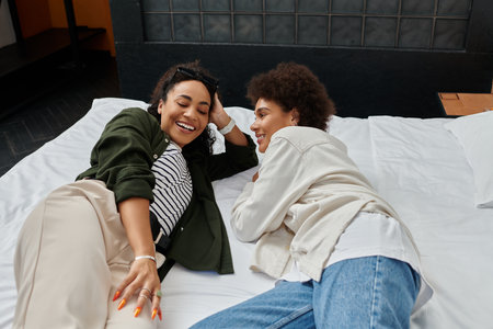 Two happy women share laughter and connection while relaxing in their cozy hotel room.の写真素材