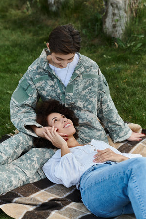A young female soldier joyfully reunites with her wife, sharing a tender moment on a grassy lawn.の写真素材