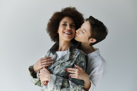 A soldier in camouflage uniform shares a loving moment with her wife in a warm studio atmosphere.の写真素材