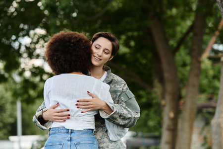 A female soldier in camouflage enjoys a heartfelt welcome from her wife in a picturesque park.の写真素材