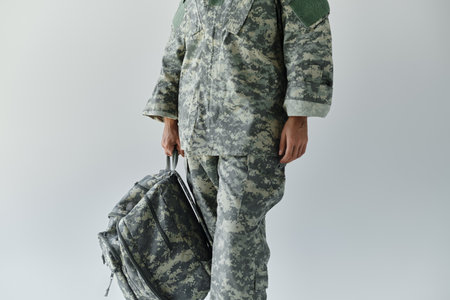 A dedicated young soldier stands confidently in camouflage gear, ready for duty with a backpack in hand.の写真素材