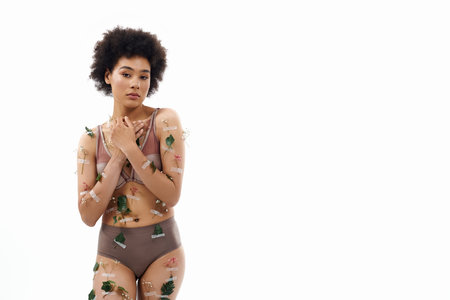 Delighted curly haired african american woman in pastel cozy underwear with flowers on body.