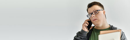 A man with Down syndrome talks on the phone while holding some files.の写真素材