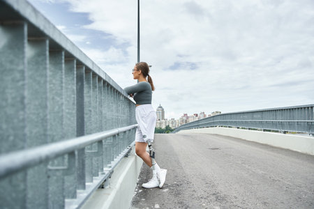 A determined young woman in sportswear engages in fitness activities on a scenic bridge.
