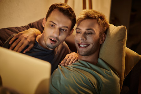 Two men enjoying a fun movie night at home, sharing smiles and laughter.の写真素材