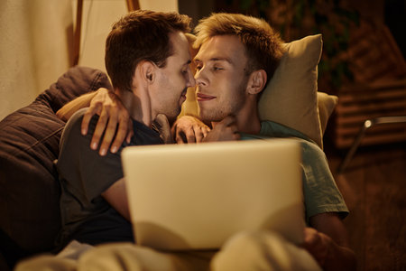 Two men share a tender moment while relaxing on the couch with a laptop.の写真素材