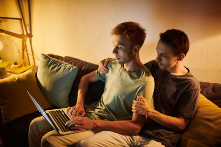 Two men share a tender moment while collaborating at home on a laptop.の写真素材